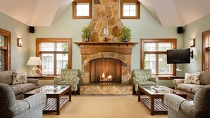 A cozy living room with a stone fireplace, comfortable seating, and a television mounted on the wall. - Anchorage by the Sea (Ogunquit)