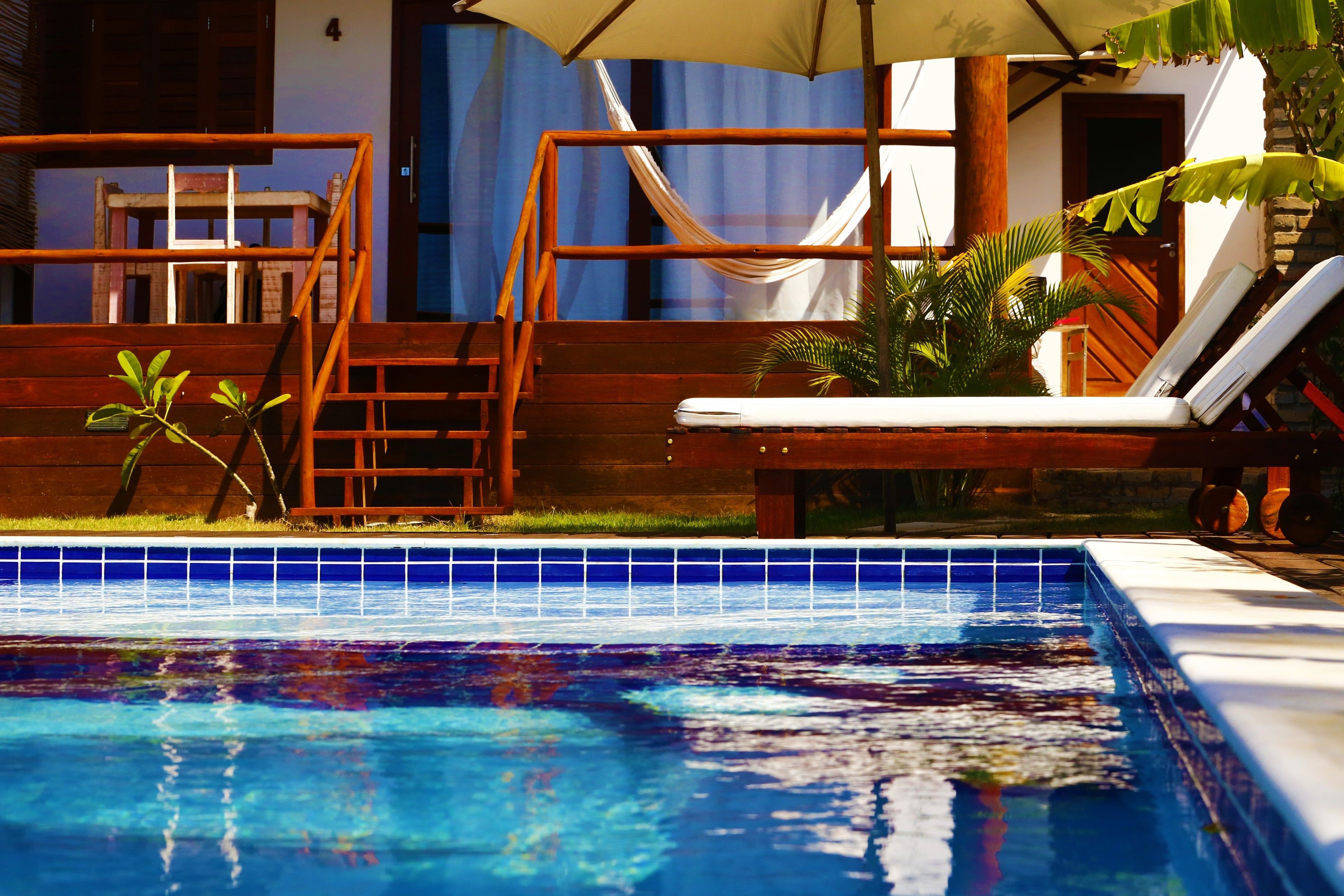 A swimming pool with a wooden deck, a hammock, and a lounge chair.