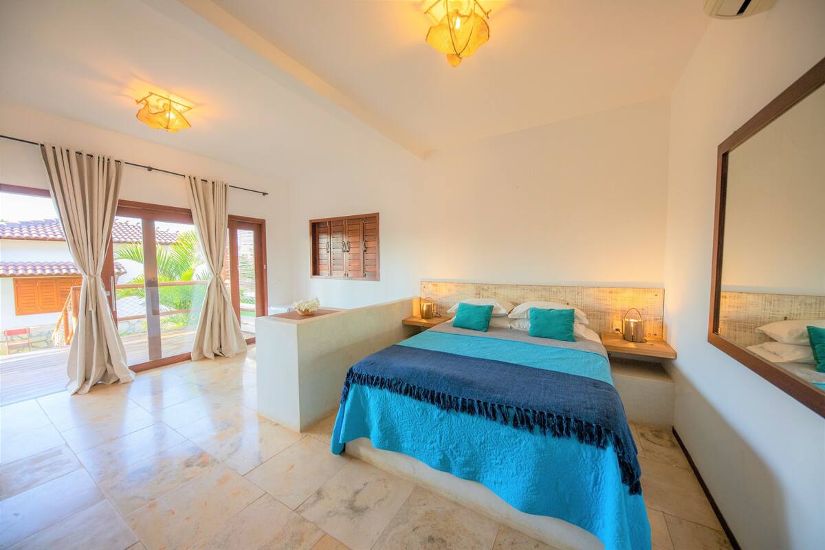 A bedroom with a bed, bedside tables, a nightstand, a window with curtains, and a view of the outside.