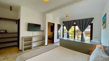 Un dormitorio con cama, televisión, armario y ventana con cortinas.