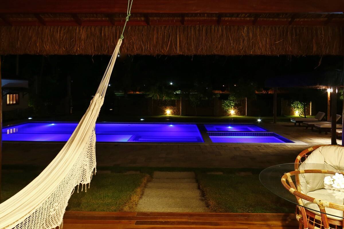 A nighttime view of a pool area with two illuminated pools, a hammock, and a wicker chair.