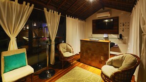 Una habitación acogedora con techo de madera, un televisor, un escritorio pequeño y dos sillones de mimbre.