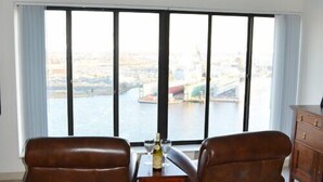 A room with two leather armchairs facing a large window with a view of a cityscape and water.