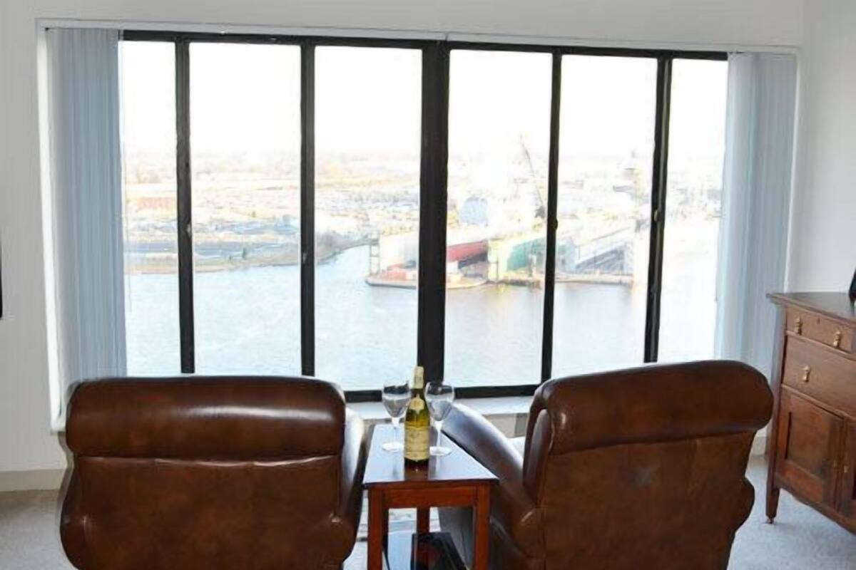Una habitación con dos sillones de cuero orientados hacia una ventana grande con vistas a un paisaje urbano y al agua.
