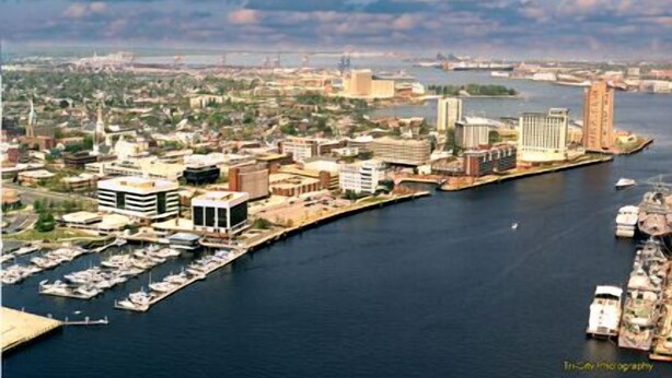 An aerial view of a coastal city with a marina, buildings, and a prominent tower.
