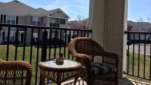 Un balcon avec des fauteuils en osier et une petite table, donnant sur un quartier résidentiel.