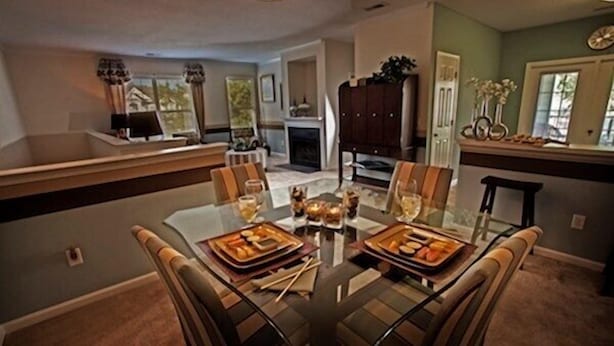 Un coin repas avec une table et des chaises en verre, une cheminée et une cuisine en arrière-plan.