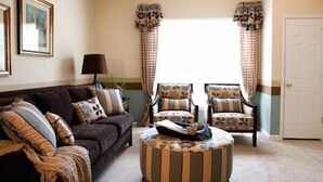 Un salon avec un canapé marron foncé, deux fauteuils à motifs, un pouf rayé et une lampe.