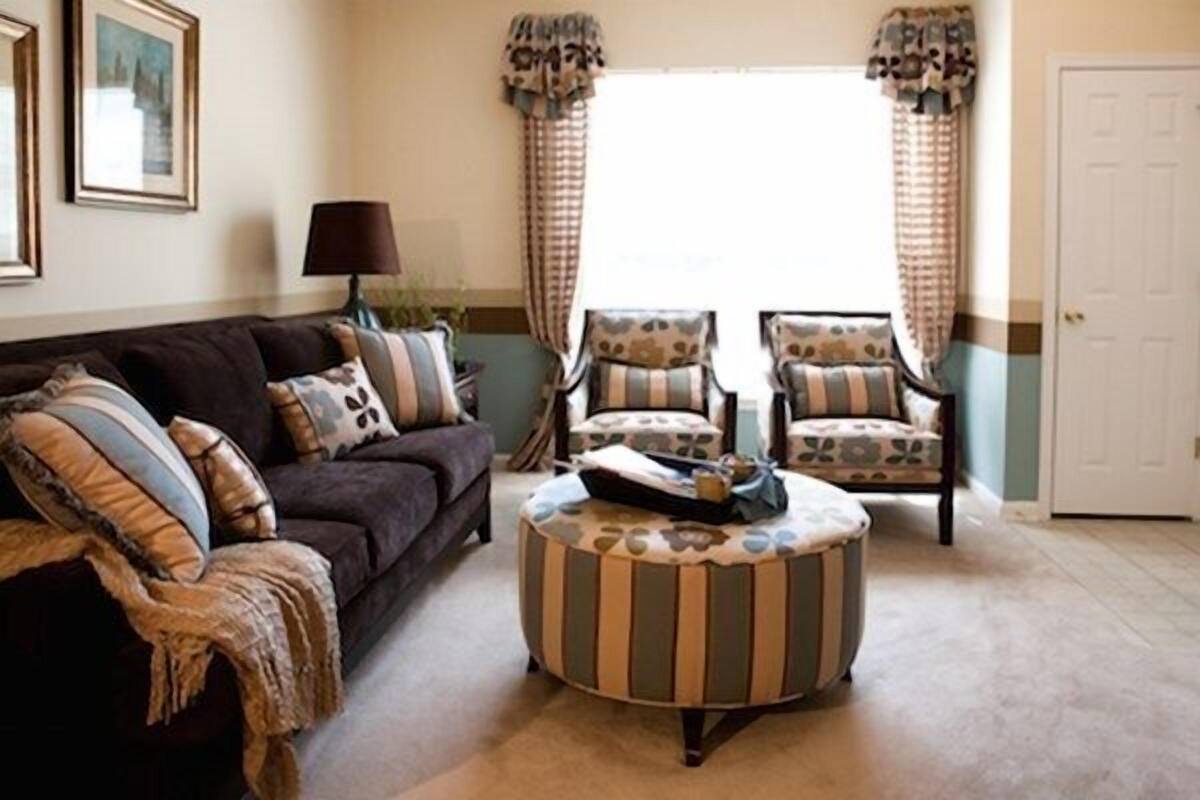 A living room with a dark brown sofa, two patterned armchairs, a striped ottoman, and a lamp.