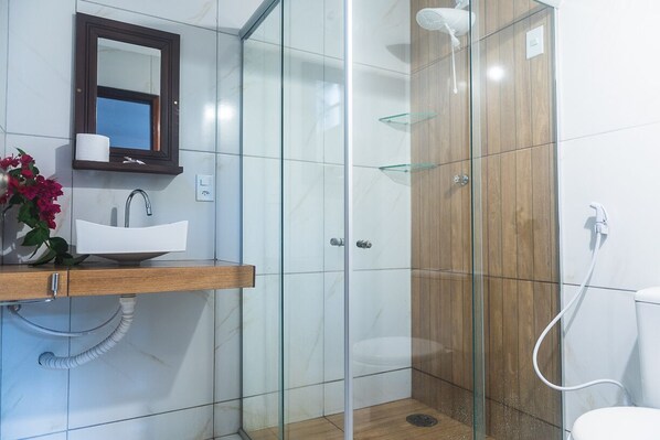 A modern bathroom with a glass shower enclosure, a wooden vanity, and a white sink. - Pousada Vila Bacana (São Miguel do Gostoso)