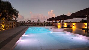 An outdoor swimming pool with a wooden deck, lounge chairs, and a thatched roof structure. - Pousada Vila Bacana (São Miguel do Gostoso)