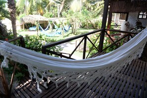 A hammock on a wooden deck with a view of a garden and a thatched-roof structure. - Pousada Vila Bacana (São Miguel do Gostoso)