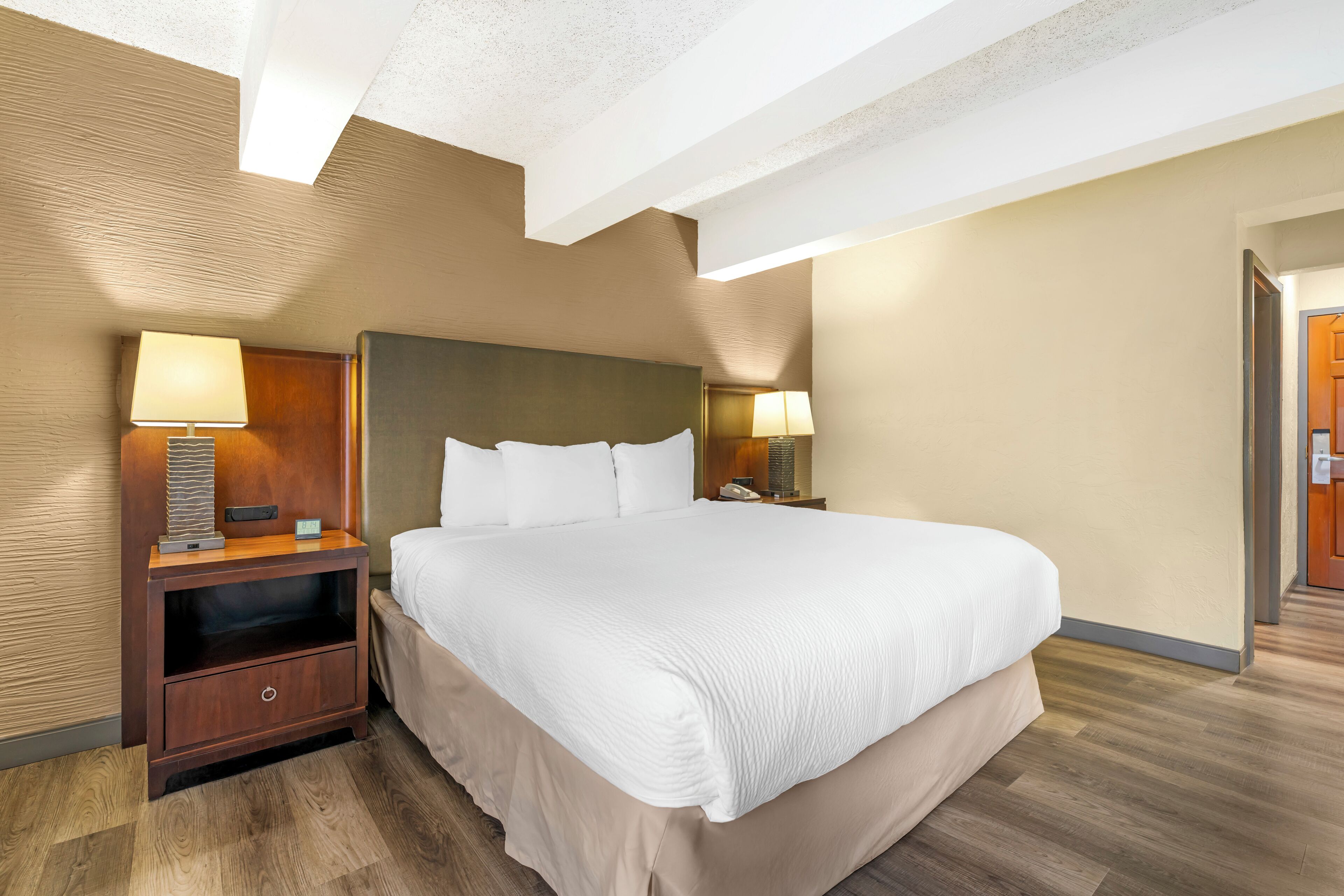 A hotel room with a large bed, wooden nightstands, and a modern ceiling design.