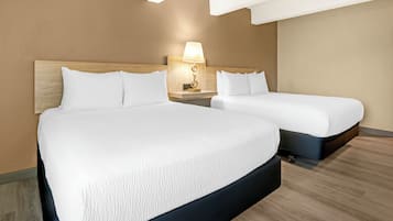 A hotel room with two beds, a wooden headboard, a nightstand with a lamp, and a wooden floor.