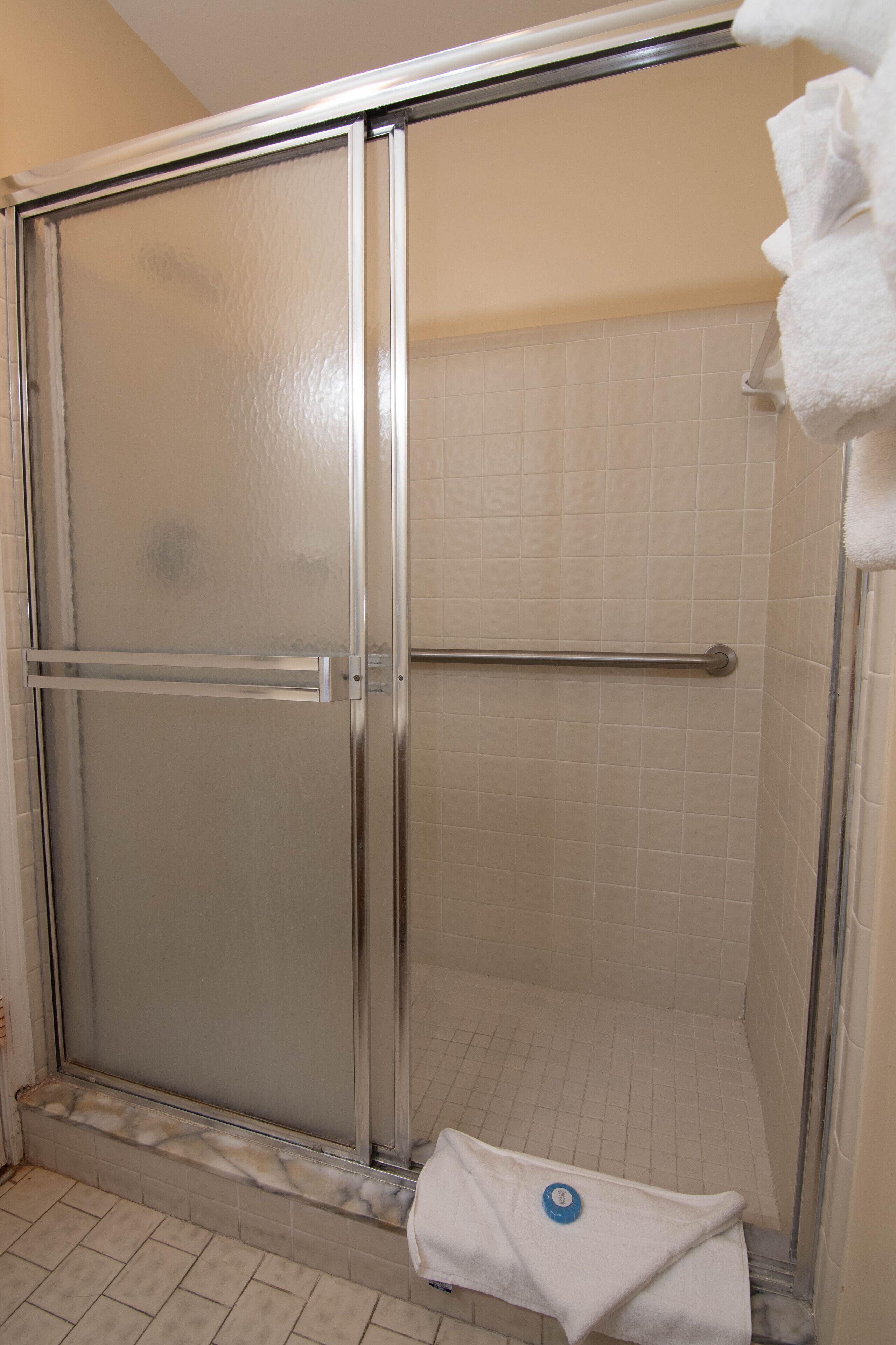 A shower with a glass door, a metal handrail, and a white towel hanging on the wall.