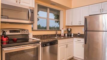 A modern kitchen with stainless steel appliances, white cabinetry, and a window providing a view of greenery outside.