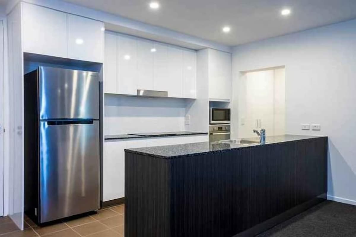 A modern kitchen with white cabinets, a stainless steel refrigerator, and a dark island.