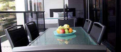 A balcony with a dining table set for two, featuring a fruit plate.