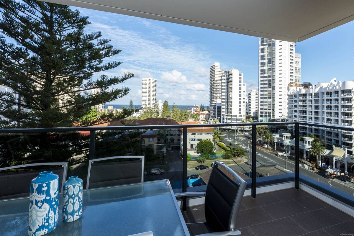 A balcony with a glass table, two patterned vases, and a view of a cityscape with tall buildings and a clear sky.