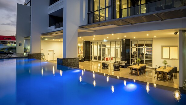 A modern hotel with a swimming pool, outdoor seating area, and a well-lit interior. - Synergy Broadbeach (Broadbeach)
