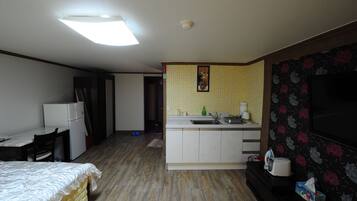 A compact kitchen with a refrigerator, sink, and a microwave. There is a dining table and a bed in the room.