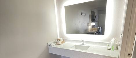 A bathroom with a large mirror, a sink, and a trash bin.