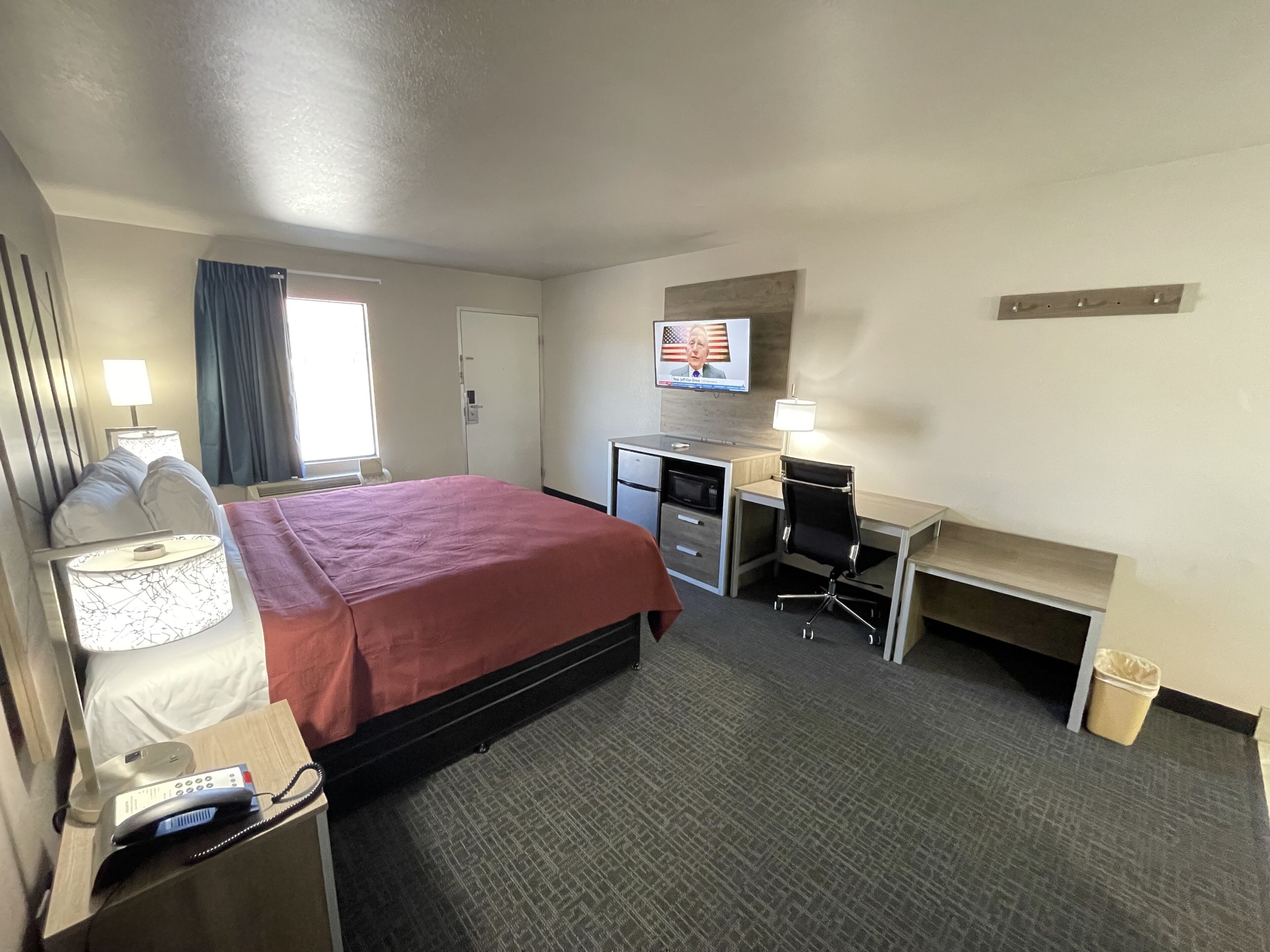 A hotel room with a bed, desk, chair, TV, and a telephone.