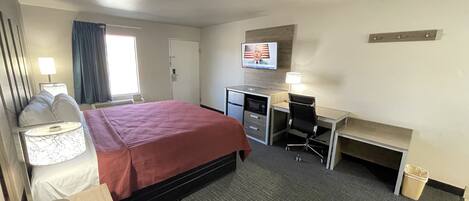 A hotel room with a bed, desk, chair, TV, and a telephone.