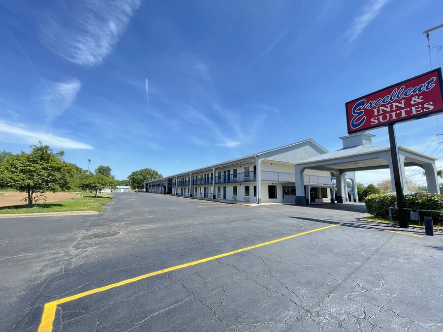 Un motel avec un ciel dégagé, un parking et une enseigne indiquant « Excellent Inn & Suites ».