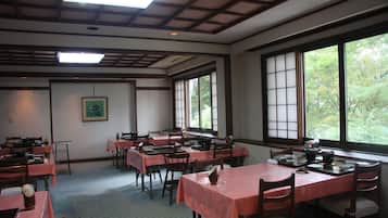A dining area with tables and chairs, large windows, and a traditional ceiling design.