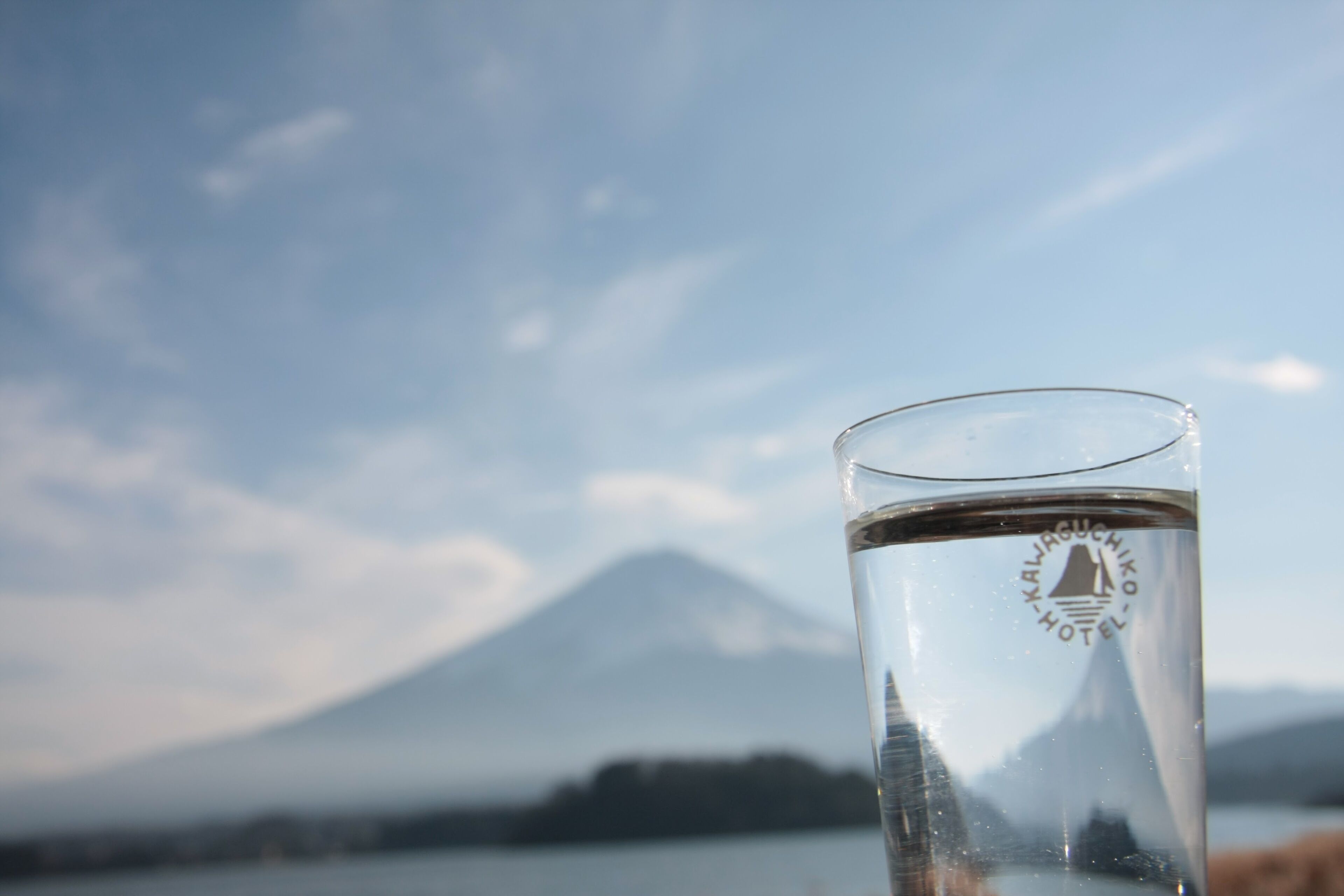 A clear glass with a logo, set against a backdrop of a mountain and a body of water.