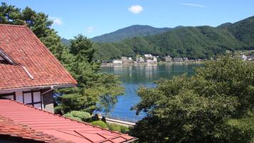 A lakeside view with a building featuring a red roof, surrounded by lush greenery and mountains in the background.