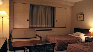 Una habitación de hotel con sofá, dos camas individuales, una mesita y una mesita de noche con lámpara.