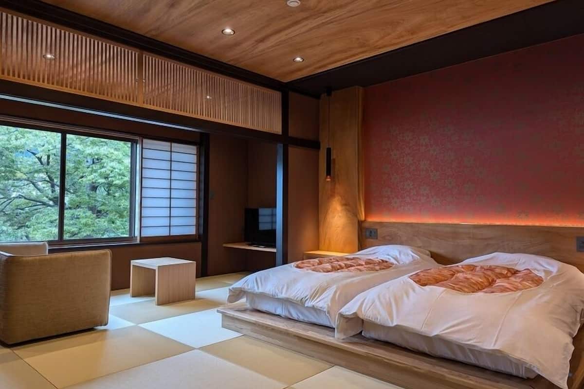 Ein modernes Hotelzimmer mit großem Fenster, zwei Betten, einer kleinen Sitzecke und einem Fernseher.