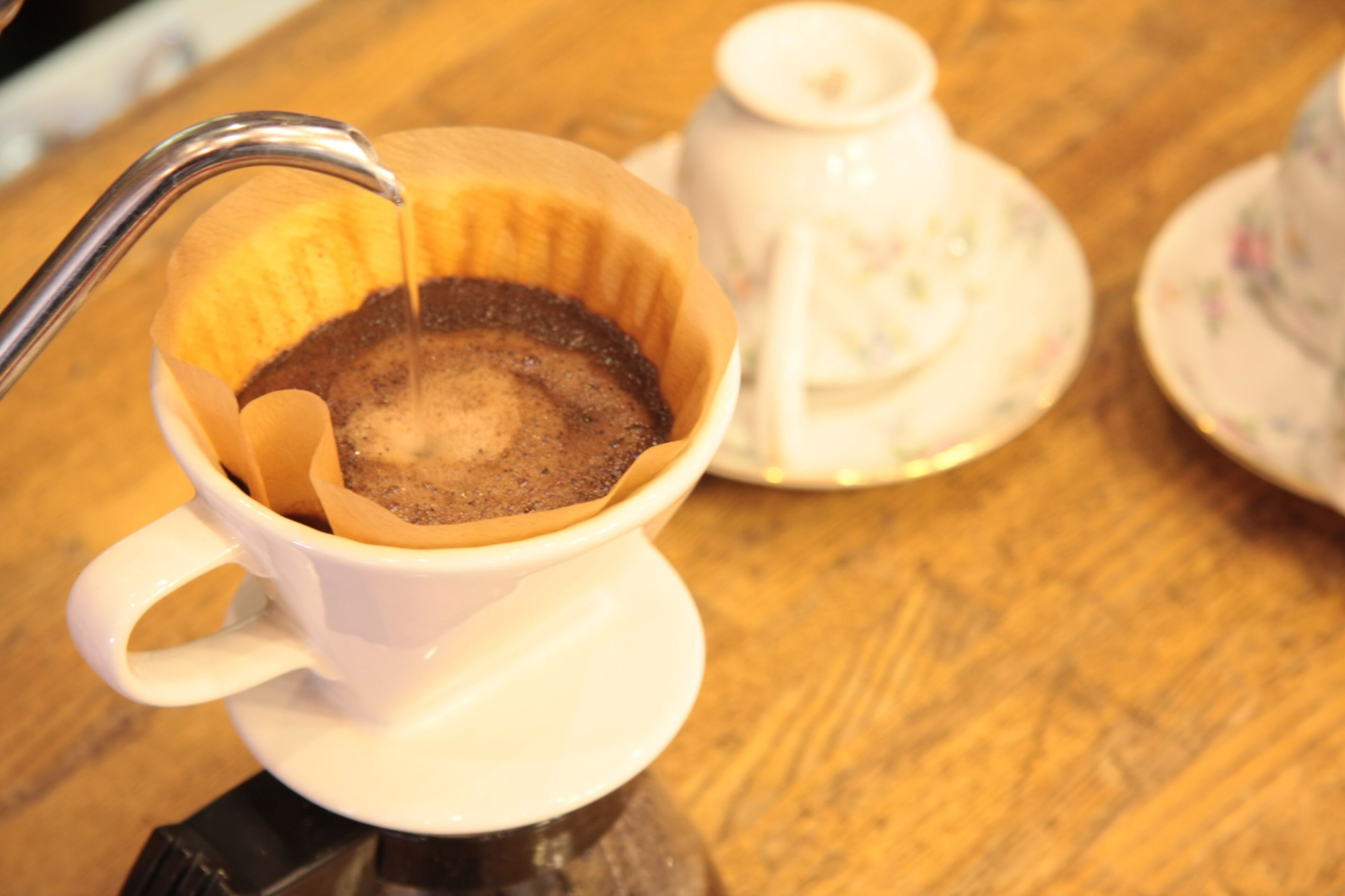 A coffee cup with a saucer and a coffee pot on a wooden table.