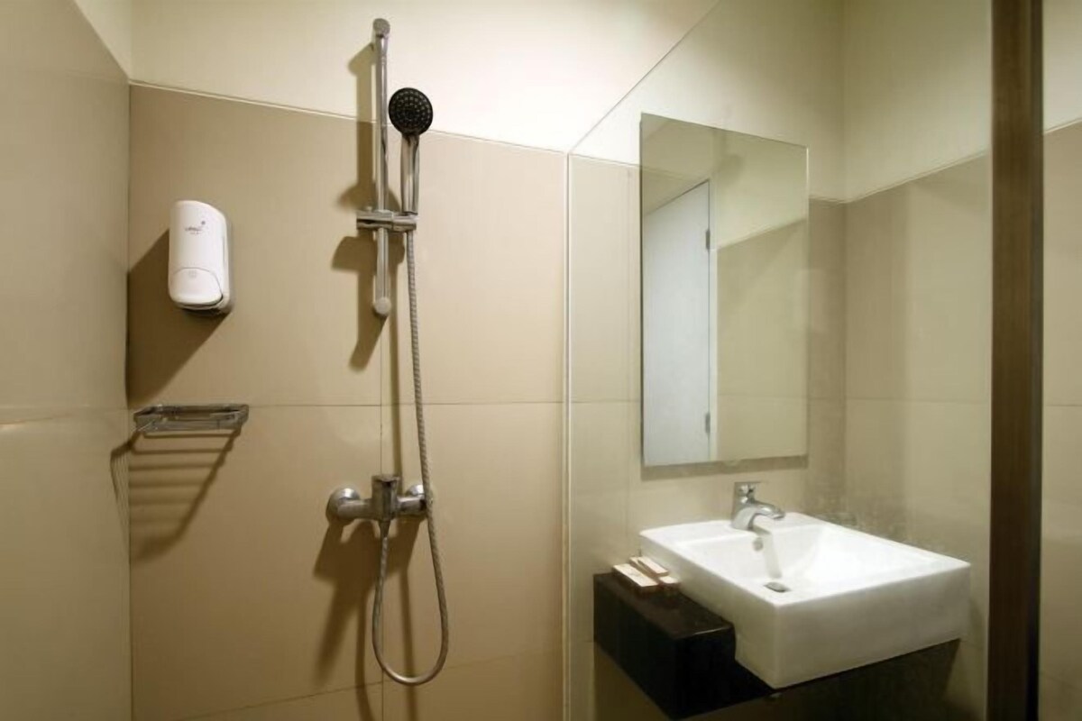Een moderne badkamer met een douche, wastafel, spiegel en zeepdispenser.