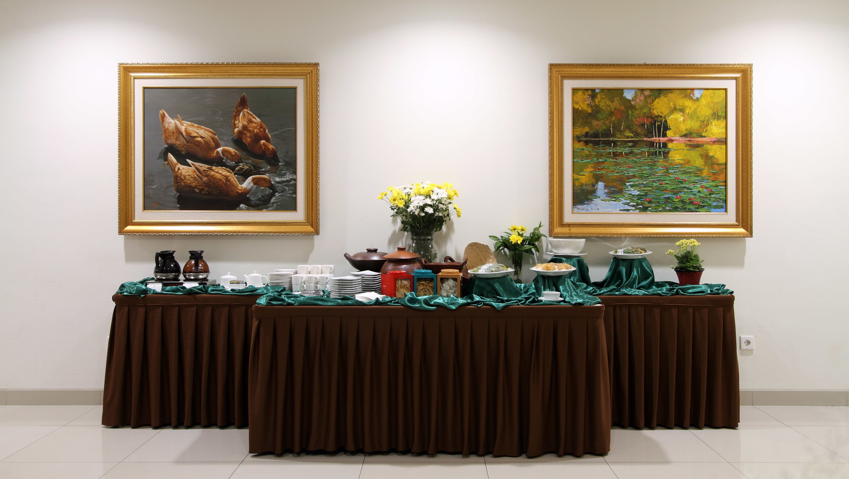A dining table with a brown tablecloth, set with plates, cups, and a vase of flowers. Two framed paintings are hung on the wall above the table.