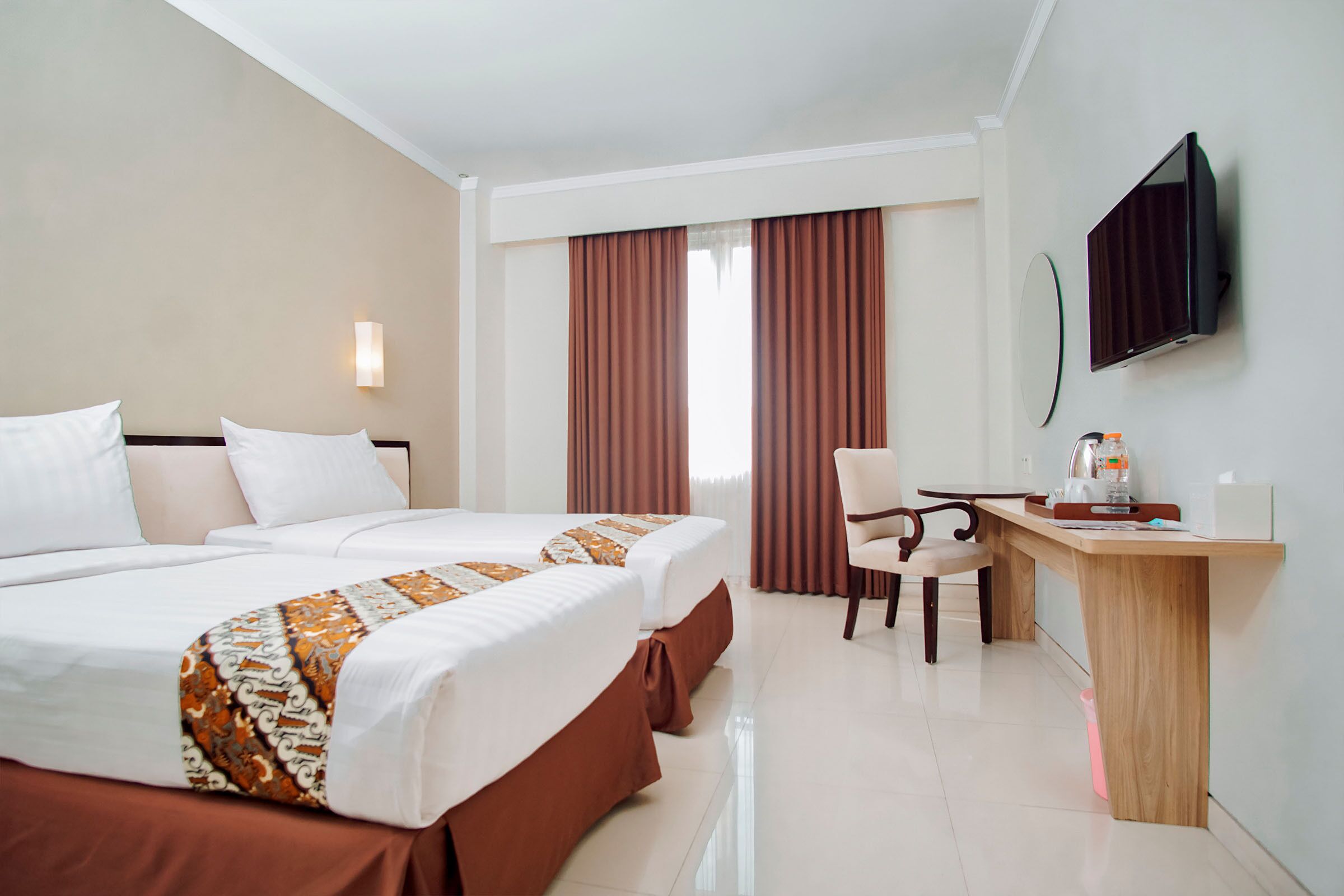 A hotel room with two beds, a desk, a chair, a television, and a window with curtains.