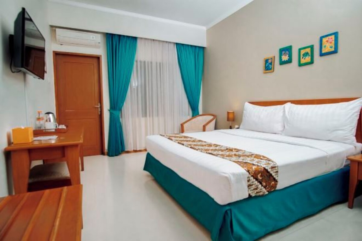 A hotel room with a bed, a desk, a chair, a television, and a window with curtains.