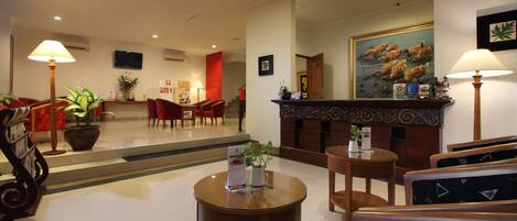 A hotel lobby with a reception desk, seating area, and a staircase leading to other floors.