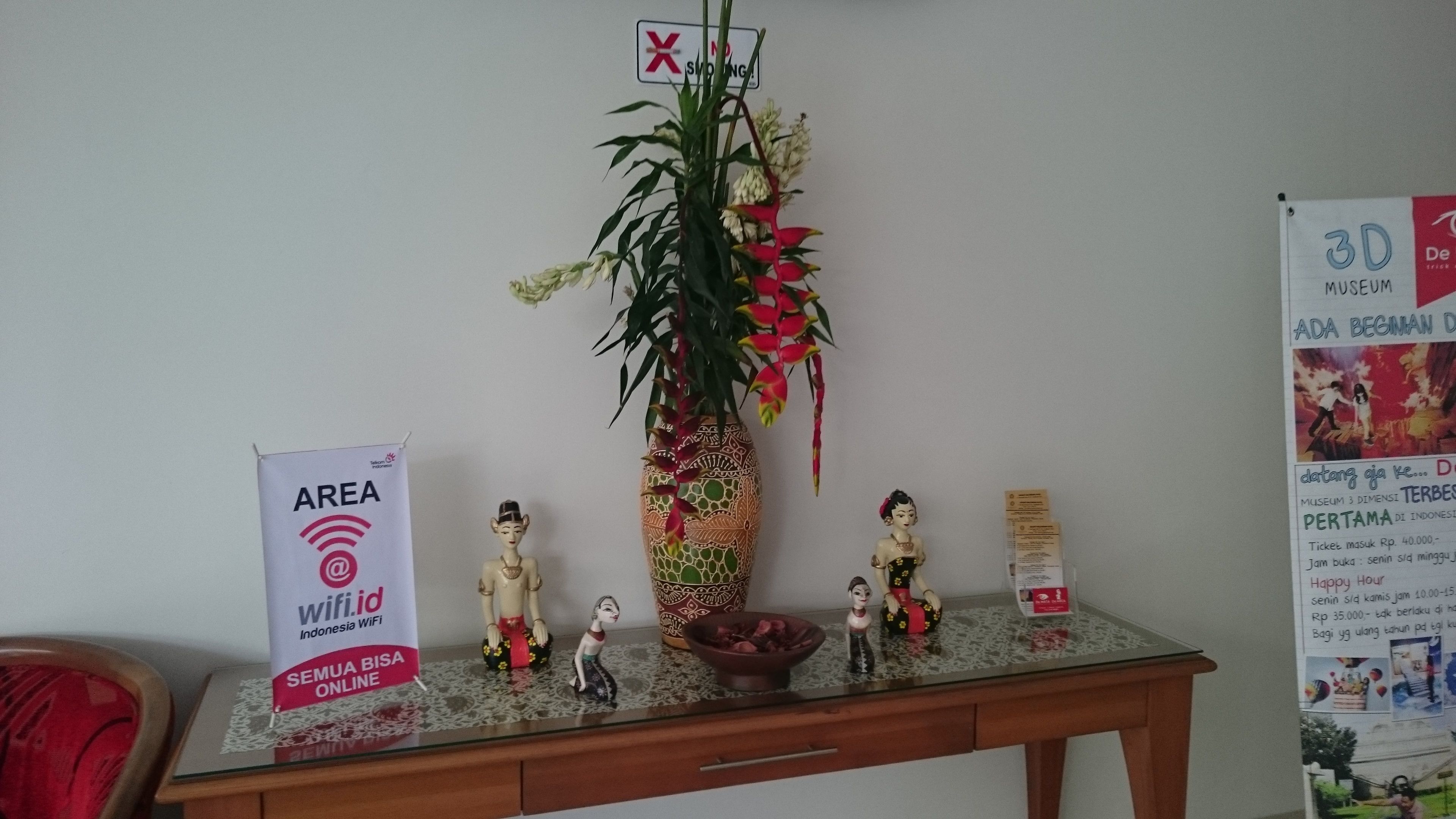 Een receptiebalie met een bordje dat een gebied voor Indonesië WiFi aangeeft, een decoratieve vaas met bloemen en een kleine verzameling beeldjes.