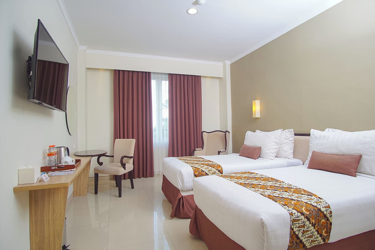 Habitación de hotel con dos camas, un escritorio, una silla, un televisor y una ventana con cortinas.