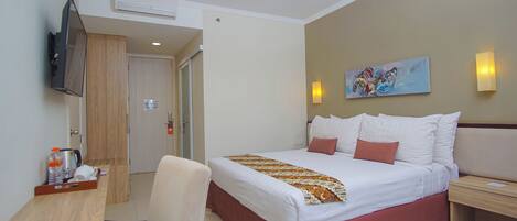 Habitación de hotel con cama, escritorio con silla, televisor montado en la pared y un cuadro sobre la cama.