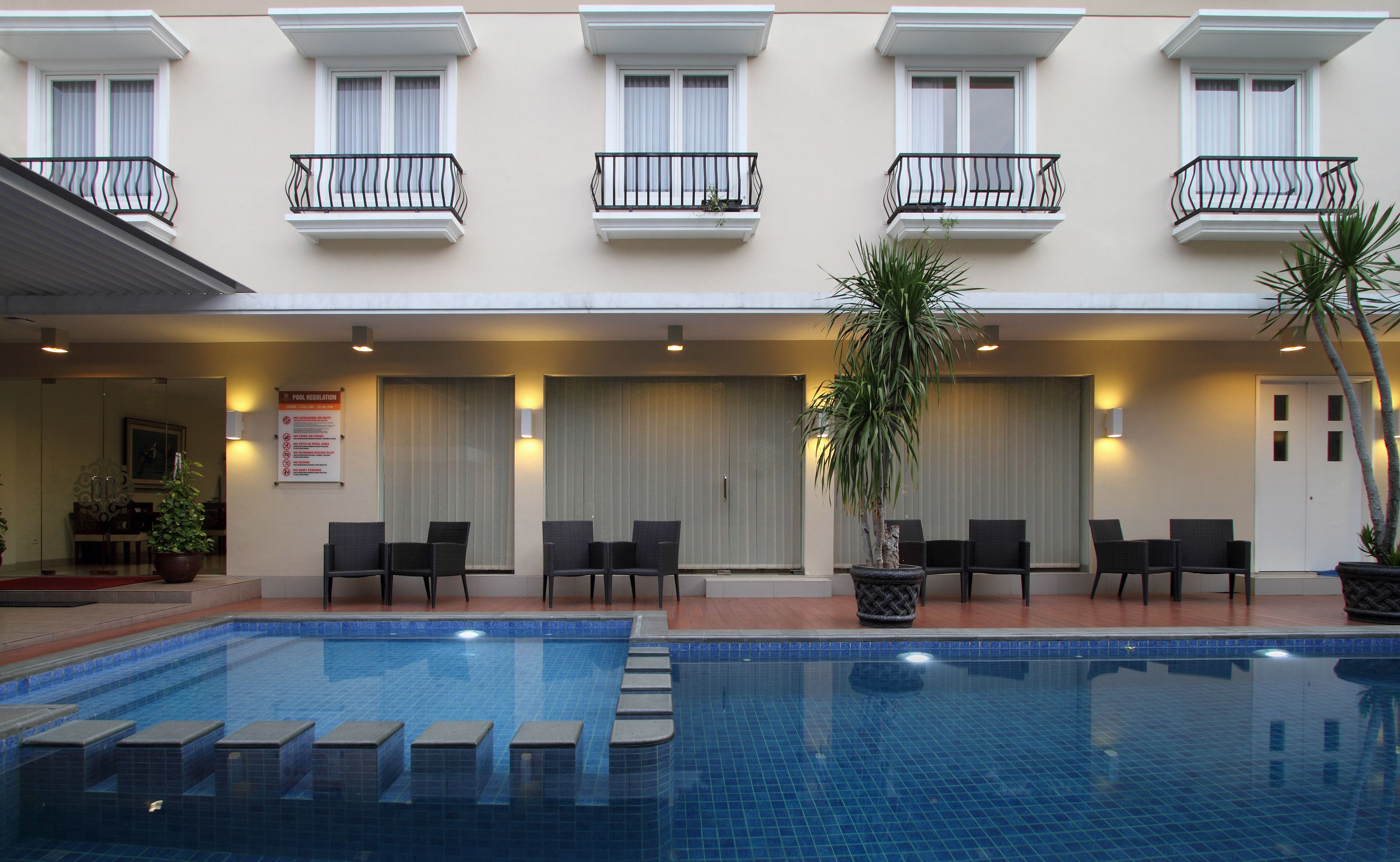 A hotel with a swimming pool, outdoor seating, and a sign indicating pool regulations.