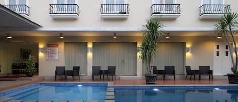 A hotel with a swimming pool, outdoor seating, and a sign indicating pool regulations.