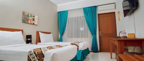 A hotel room with two beds, a desk, a television, and a window with curtains.