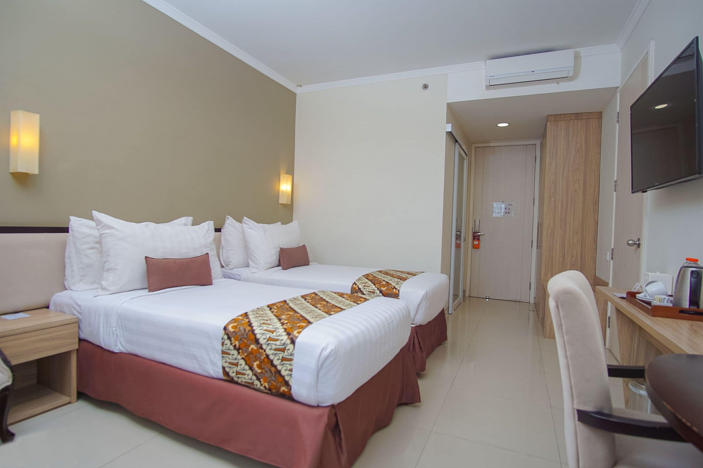 A hotel room with two beds, a desk, a chair, a TV, and a wardrobe.