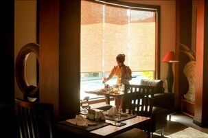 A dining area with a table set for two, a chair, and a window with a view of the outdoors.