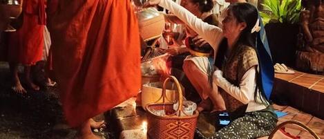 Un moine vêtu d’une robe orange échange avec des personnes devant un bâtiment sur lequel on peut lire l’inscription « SALAM ».
