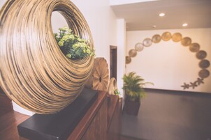 A modern interior with a large, circular, textured sculpture on a wooden base, a potted plant, and a decorative wall with circular elements.